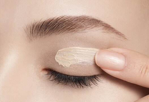 Close-up of a young woman applying concealer or eyelid primer with her finger