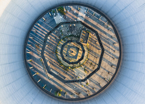 Aerial view of an abandoned circular industrial structure with concentric geometry, dramatic long shadows and nature slowly reclaiming the decaying infrastructure in Italy.