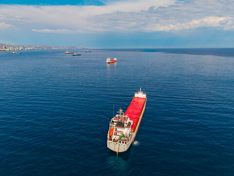 Aerial view of a cargo ship with a red deck anchored in the Mediterranean Sea near the coast of Lemesos, Lemesos, Cyprus.