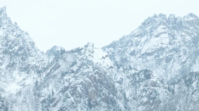 Natural Rock Mountain Cliffside With Exposed Rocky Surfaces And Patches Of Snow Across The Rugged Terrain. Tracking Shot