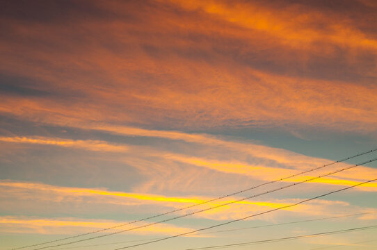 Dramatic sunset sky landscape background. Bright golden and orange clouds and diagonal power lines silhouetted against the colorful evening atmosphere