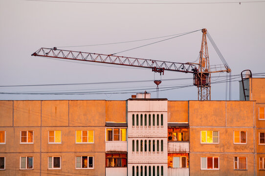 Urban architecture background. A construction crane above residential buildings. Warm sunset light on the brick facades and windows of the city structure