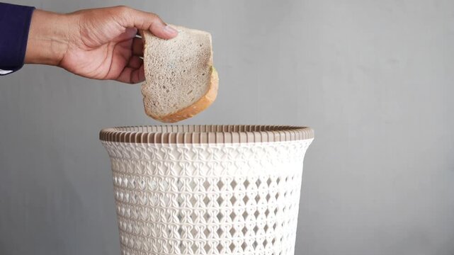 Close up slow motion footage of hand throwing moldy bread in a trash bin, concept of food waste and decaying food