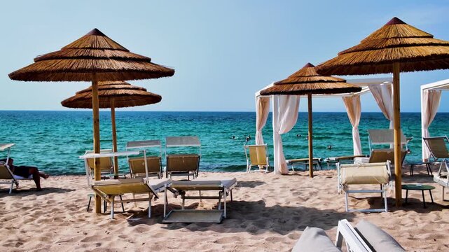 Panoramic view of the beach with umbrellas and wooden armchairs overlooking the turquoise Mediterranean Sea in sunny Italy