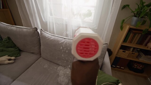 African American father shooting soap bubbles from POV perspective at cheerful young son playing behind sofa. Footage is ideal for family lifestyle campaigns and parenting commercials
