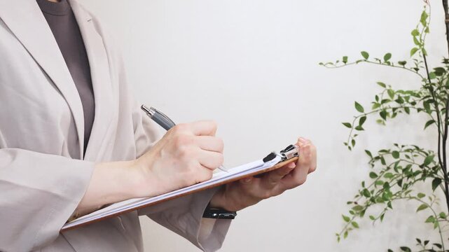 クリップボードの書類に記入する人の手元