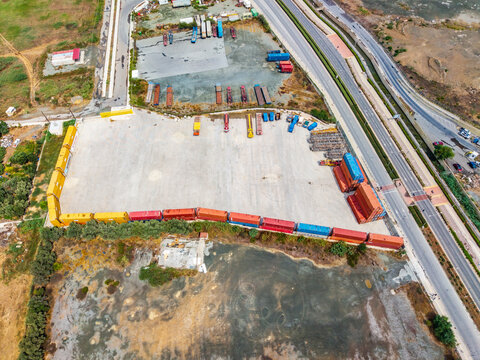 Aerial view of a shipping container yard with rows of colorful containers, adjacent to a highway and open land in Lemesos, Lemesos, Cyprus.