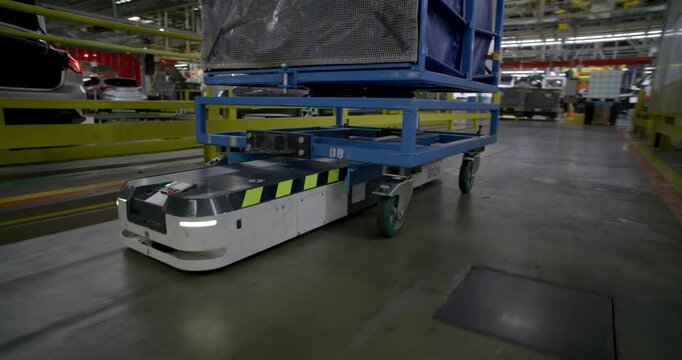 Autonomous mobile robot transporting a heavy blue cargo rack through a large industrial warehouse facility	