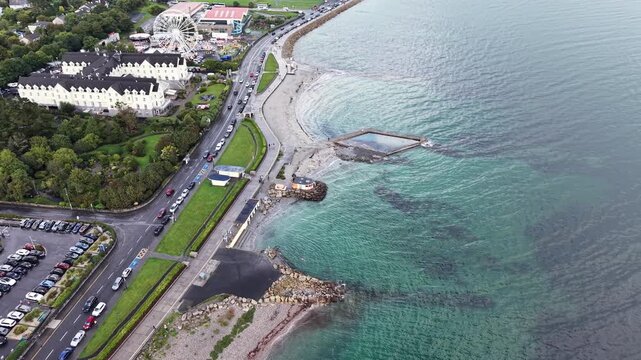 Aerial drone footage overlooking the Salthill waterfront in Galway, Ireland. The view shows the coastal promenade, rocky shoreline, swimming area, Blackrock diving platform, busy coastal road