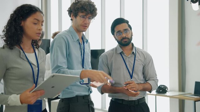 Diverse engineering professionals collaborating during a technology project discussion while reviewing information on a tablet in a modern office environment.
