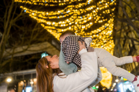 Loving mother lifting child under festive christmas lights