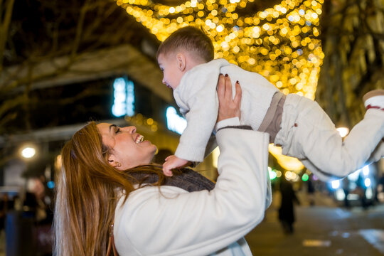 Mother lifting baby son at christmas lights street