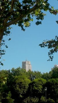 A vertical perspective of the iconic Edificio de Espana skyscraper in Madrid, framed by lush green trees and a clear blue sky. Perfect for travel and urban lifestyle content.