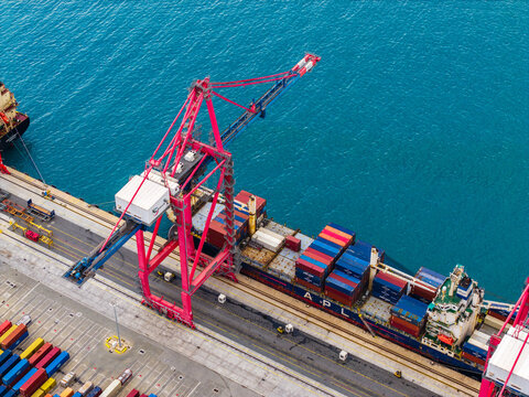 Aerial view of a large container ship being loaded by a bright red gantry crane at the busy Limassol Port in Lemesos, Lemesos, Cyprus.