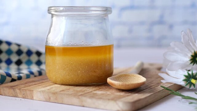 Ghee in glass jar on wooden board next to a small wooden spoon and white flowers with copy space
