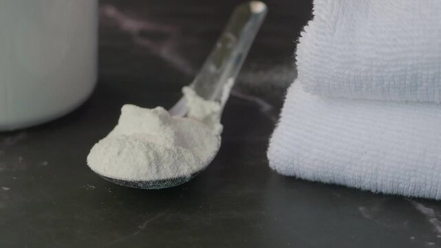 Close up slow motion of washing powder on spoon with white towels, clean laundry essentials, household chores and cleanliness