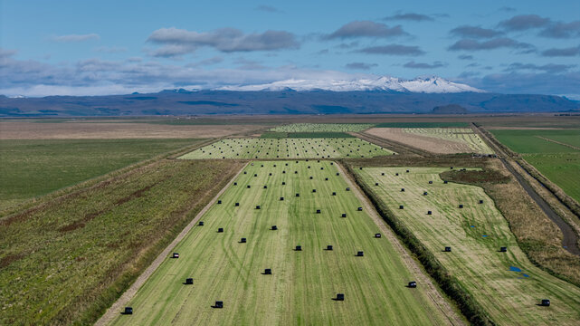 Aerial view of farmland with wrapped haylage bales in fields under a blue sky in Rangarthing eystra, Iceland.