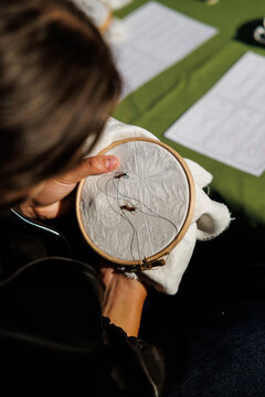 Close-up of a person holding an embroidery hoop with light fabric, dark thread, and small insect motifs during a hands-on outdoor craft activity