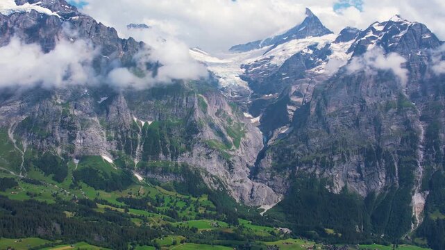 Cinematic drone fly over breathtaking view of Grindelwald surrounded by towering mountain peaks and lush green valleys. Snow-capped summits and scattered cloud. Travel and healthy lifestyle