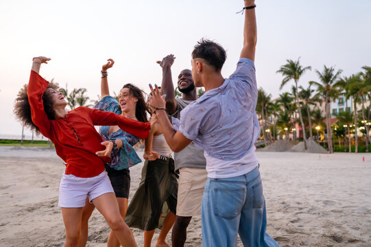 Joyful summer beach party with multiethnic friends celebrating vacation, enjoying music, freedom