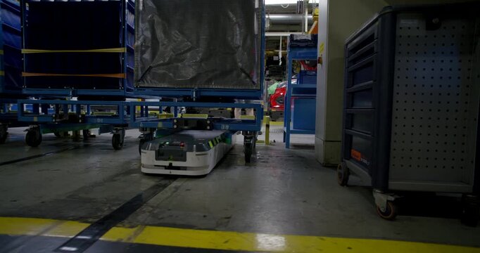 Autonomous mobile robot transporting a heavy blue cargo rack through a large industrial warehouse facility	