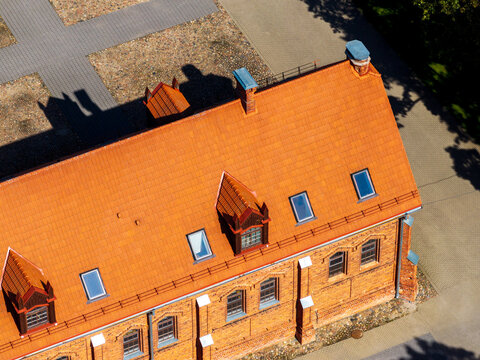 Aerial view of the historic red brick Raudondvaris Manor with its orange tiled roof, dormer windows, and skylights set within a paved courtyard in Raudondvaris, Kauno apskritis, Lithuania.