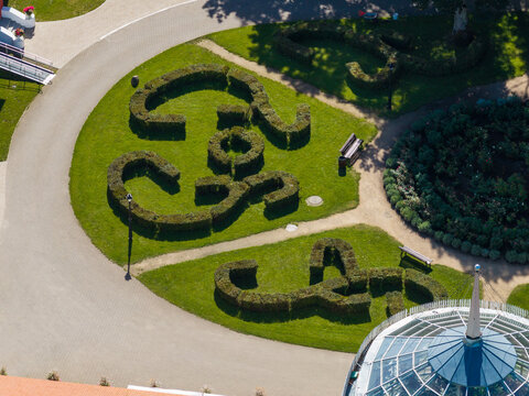 Aerial view of Raudondvaris Manor featuring intricate topiary hedges, manicured lawns, winding pathways, and a glass greenhouse in Raudondvaris, Kauno apskritis, Lithuania.