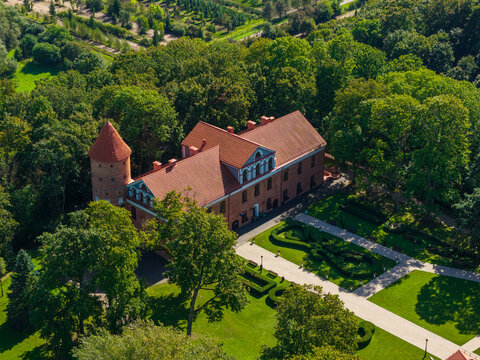 Aerial view of Raudondvaris Manor with red brick architecture, round tower, and manicured gardens surrounded by lush trees in Raudondvaris, Kauno apskritis, Lithuania.