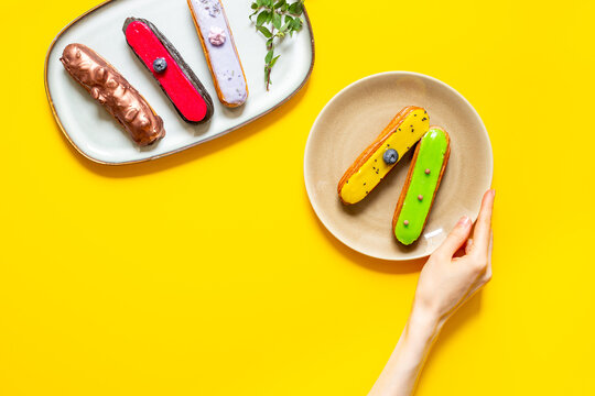 Hand serving colorful eclairs on plate - cozy dessert sharing moment with elegant French pastries, top view