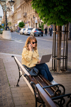 Confident mature woman with laptop sitting on the street in a European city