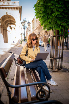 Confident mature woman with laptop sitting on the street in a European city