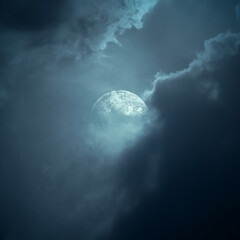 Full moon glowing through dramatic dark storm clouds in a moody blue night sky. Smoke background
