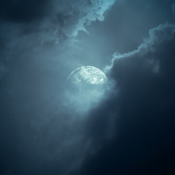 Full moon glowing through dramatic dark storm clouds in a moody blue night sky. Smoke background