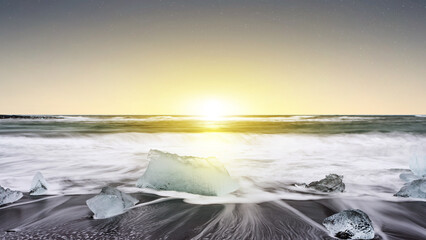 Glacial ice blocks scattered on the black sand beach of Diamond Beach in Iceland during a golden sunset, with ocean waves washing over the shore. Morning scene background © Leo Lintang