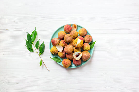Fresh lychee fruit with green leaves on a plate, top view