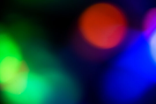 Abstract blurred bokeh background with colorful vibrant glowing circular lights on a dark backdrop. Abstract holiday illumination and decoration background