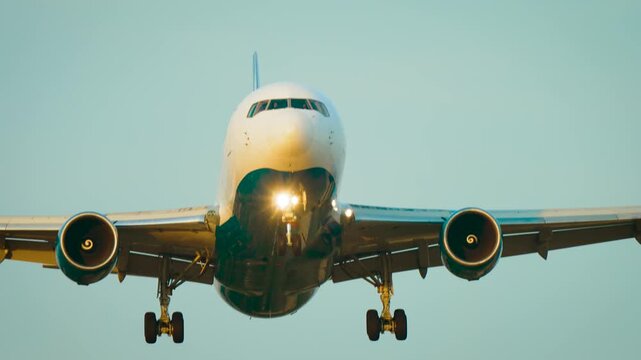 Jet Airliner Front View. Twin engine passenger aircraft approaching runway with illuminated landing lights. Civil aviation travel transport during final landing approach under blue sky