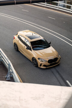 ew BMW 1 Series in a refined sand beige finish parked on asphalt beneath a modern city bridge highlighting compact proportions, sharp design, premium details and contemporary German automotive styling