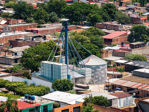 Aerial view of Industrias Pecuarias de Tuxpan S.A. de C.V. with a blue grain elevator and metal silos surrounded by residential rooftops and lush trees in Tuxpan, Jalisco, Mexico.