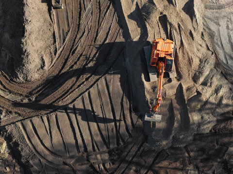 Aerial view of an orange excavator working on a sandy construction site with deep tire tracks in the soil, Enschede, Overijssel, Netherlands.