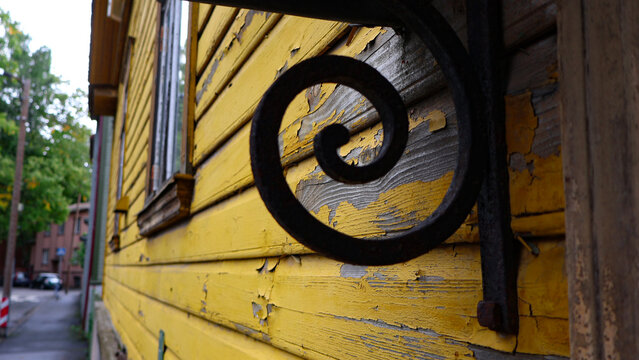 Old yellow wooden facade with peeling paint and decorative wrought iron scroll, weathered texture and cracked, worn surfaces showing vintage decay and the passage of time