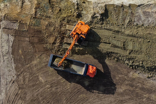 Aerial view of an orange excavator loading soil into a dump truck at a construction site in Enschede, Overijssel, Netherlands.