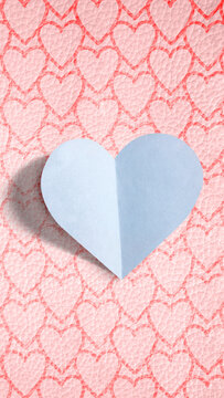 A blue folded paper heart on a pink background patterned with smaller hearts. Love background