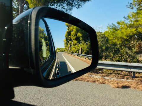 Road reflected in car side mirror, tree-lined highway