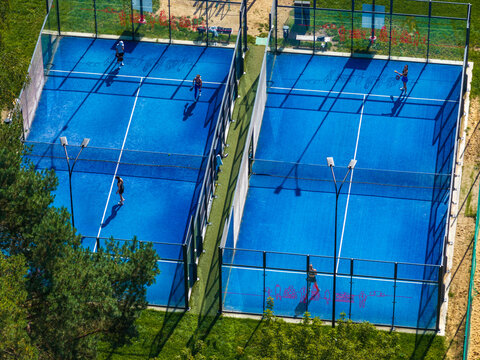 Aerial view of two blue padel courts with players in action, surrounded by green trees and grass in Vilnius, Vilnius County, Lithuania.