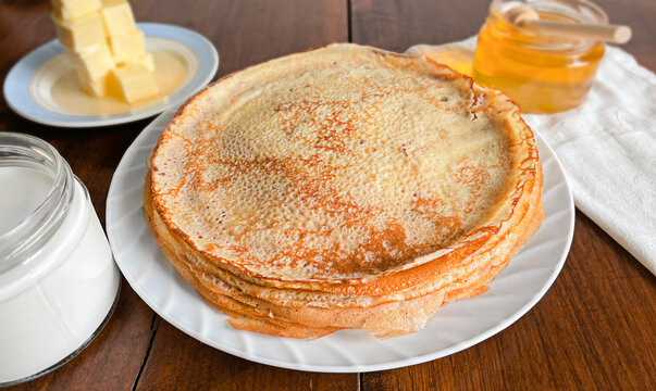 Rustic still life: traditional breakfast with a stack of homemade pancakes, honey, butter, and milk on a wooden table with linen napkin. Maslenitsa and Shrove Tuesday celebration concept.