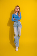 Fototapeta premium Smiling blonde woman posing casually in stylish outfit on vibrant yellow background, suitable for fashion and lifestyle concepts