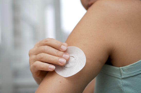 Close-up of a female patient attaching a continuous glucose monitoring sensor to the back of her upper arm using an automatic applicator at home.