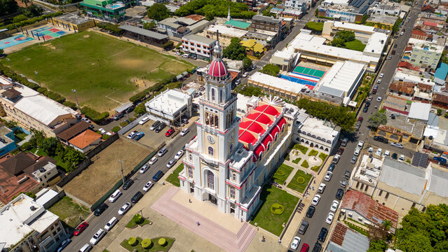Aerial view of the Iglesia Sagrado Corazon de Jesus with its distinctive red roof and white facade, surrounded by urban streets and buildings in Moca, Espaillat Province, Dominican Republic.