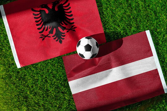 Albania vs. Latvia football match. National flags on green grass with soccer ball in the middle. Football background for international match.